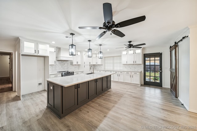 kitchen with wall chimney exhaust hood, sink, white cabinets, a barn door, and an island with sink