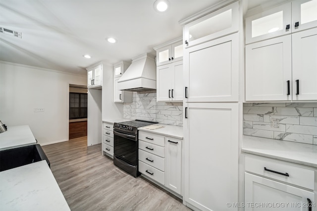 kitchen featuring custom exhaust hood, white cabinets, tasteful backsplash, and range with electric stovetop