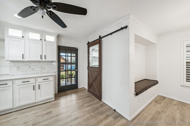 interior space featuring crown molding, light hardwood / wood-style flooring, tasteful backsplash, white cabinetry, and a barn door