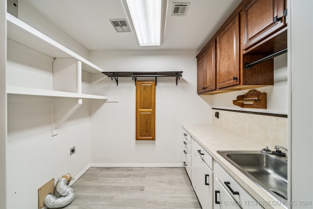 clothes washing area with sink, hookup for an electric dryer, light hardwood / wood-style floors, and cabinets