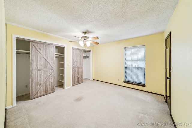 unfurnished bedroom with light carpet, a textured ceiling, ceiling fan, and a barn door