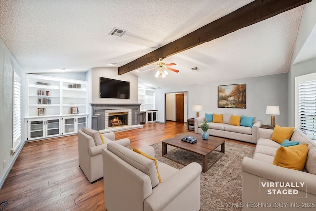 living room with built in features, lofted ceiling with beams, a fireplace, hardwood / wood-style floors, and a textured ceiling