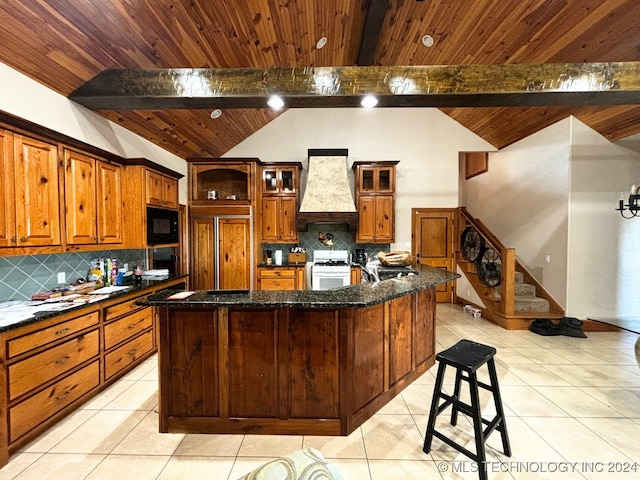 kitchen featuring premium range hood, dark stone counters, a large island with sink, white range with gas stovetop, and black microwave