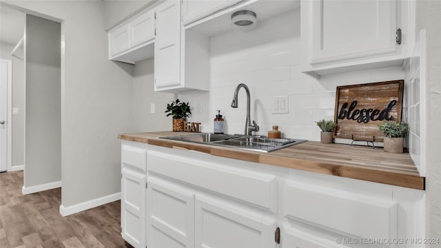 kitchen with light wood-type flooring, white cabinetry, butcher block counters, and sink