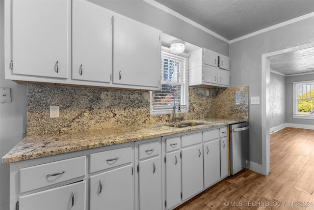 kitchen with decorative backsplash, white cabinets, crown molding, hardwood / wood-style flooring, and dishwasher