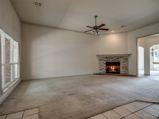 unfurnished living room with ceiling fan, a stone fireplace, light colored carpet, and ornamental molding