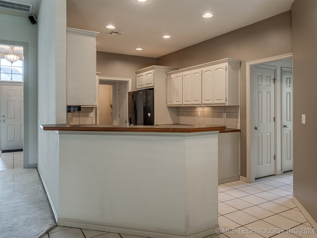 kitchen featuring light tile patterned floors, black fridge, kitchen peninsula, decorative backsplash, and white cabinets