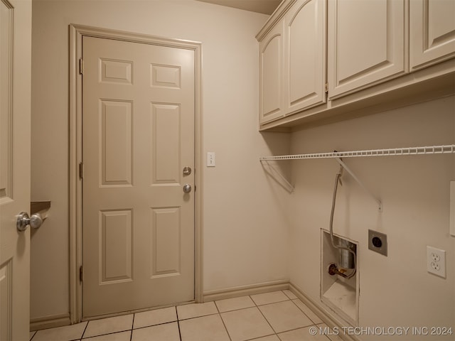 laundry area featuring electric dryer hookup, cabinets, and light tile patterned floors