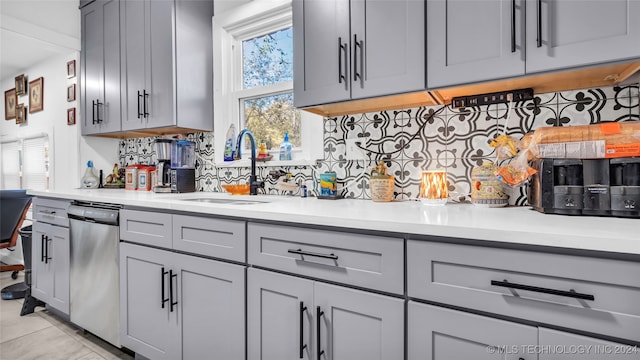 kitchen featuring gray cabinetry, sink, stainless steel dishwasher, backsplash, and light tile patterned flooring