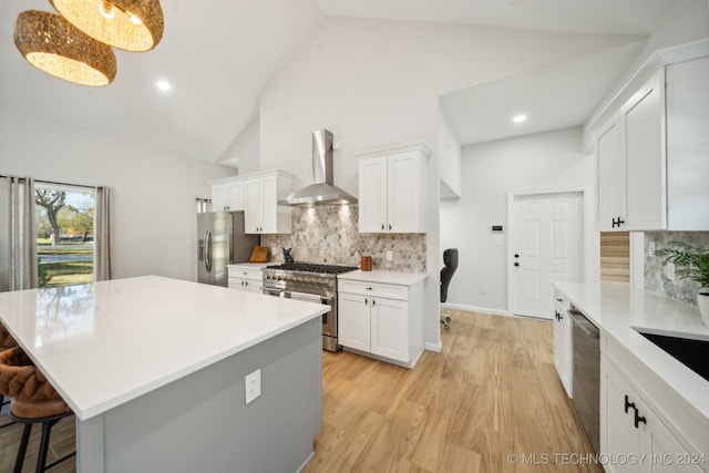 kitchen featuring hanging light fixtures, white cabinets, stainless steel appliances, and wall chimney range hood