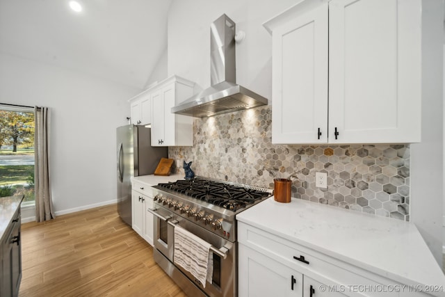 kitchen featuring wall chimney range hood, vaulted ceiling, light wood-type flooring, white cabinetry, and stainless steel appliances