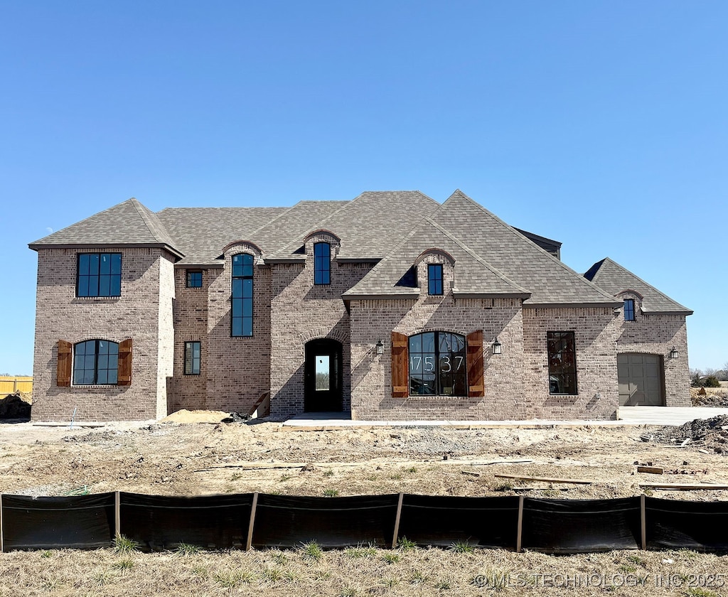 french country home featuring brick siding, a garage, and roof with shingles