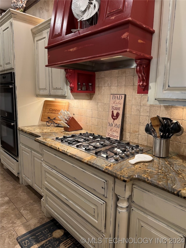 kitchen with dark stone countertops, double oven, tasteful backsplash, custom range hood, and stainless steel gas cooktop