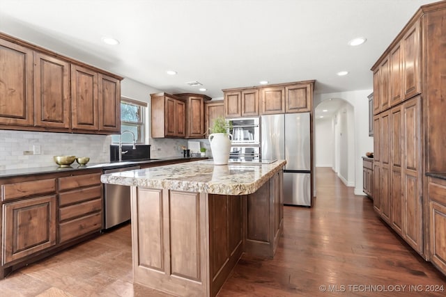 kitchen with appliances with stainless steel finishes, backsplash, sink, wood-type flooring, and a kitchen island