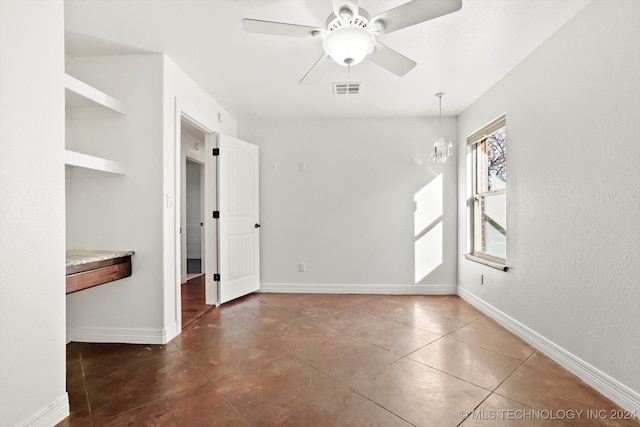 unfurnished room with ceiling fan with notable chandelier and dark tile patterned floors