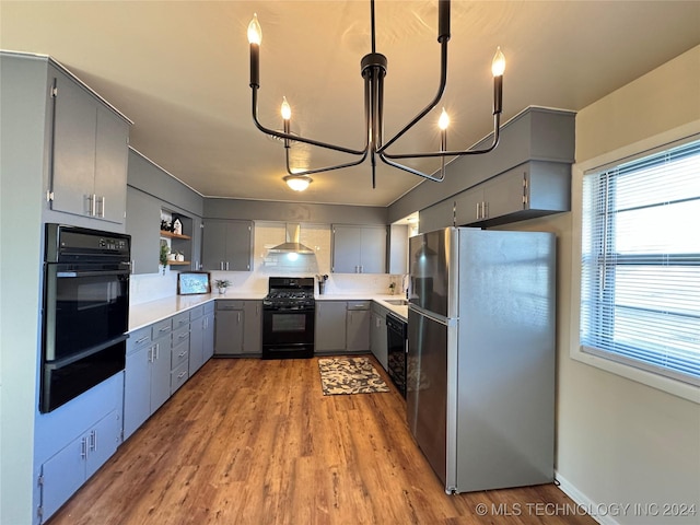 kitchen featuring gray cabinetry, decorative light fixtures, black appliances, and wall chimney exhaust hood