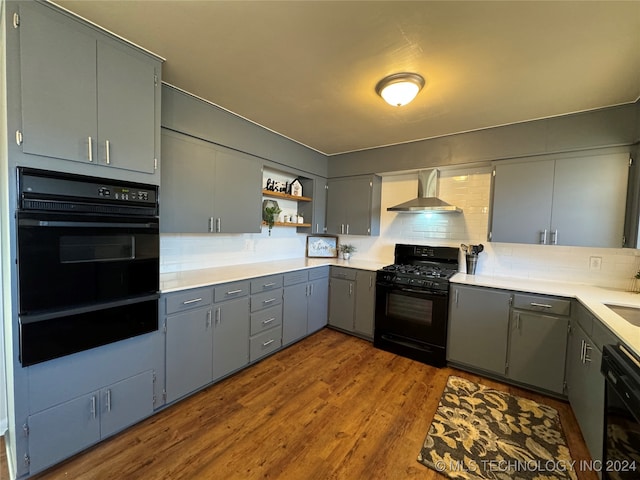 kitchen with gray cabinetry, wall chimney range hood, light hardwood / wood-style flooring, decorative backsplash, and black appliances