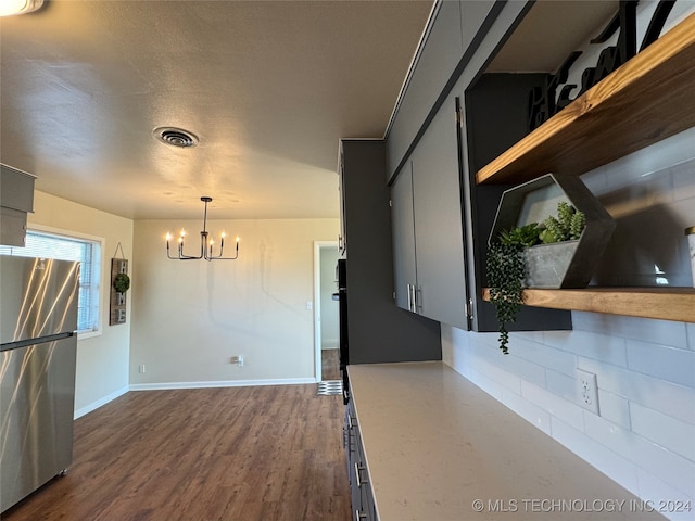 kitchen with an inviting chandelier, dark hardwood / wood-style flooring, backsplash, stainless steel fridge, and pendant lighting