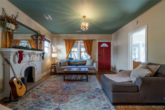 living room featuring crown molding, wood-type flooring, a notable chandelier, and a brick fireplace