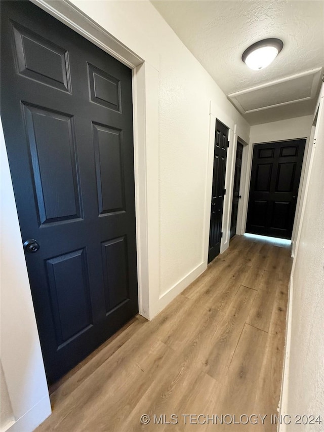 corridor with light wood-type flooring and a textured ceiling