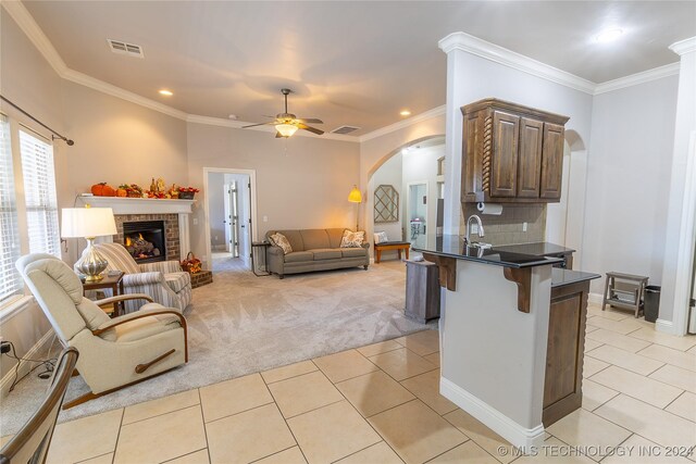 kitchen with a brick fireplace, a kitchen breakfast bar, kitchen peninsula, light colored carpet, and ornamental molding