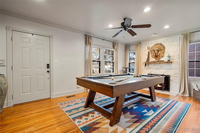 game room featuring a stone fireplace, crown molding, billiards, ceiling fan, and light wood-type flooring