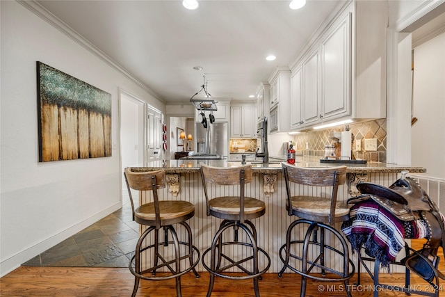 kitchen with kitchen peninsula, a kitchen bar, tasteful backsplash, crown molding, and white cabinetry