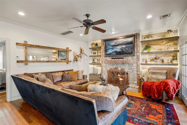 living room with a brick fireplace, built in shelves, ceiling fan, crown molding, and hardwood / wood-style flooring