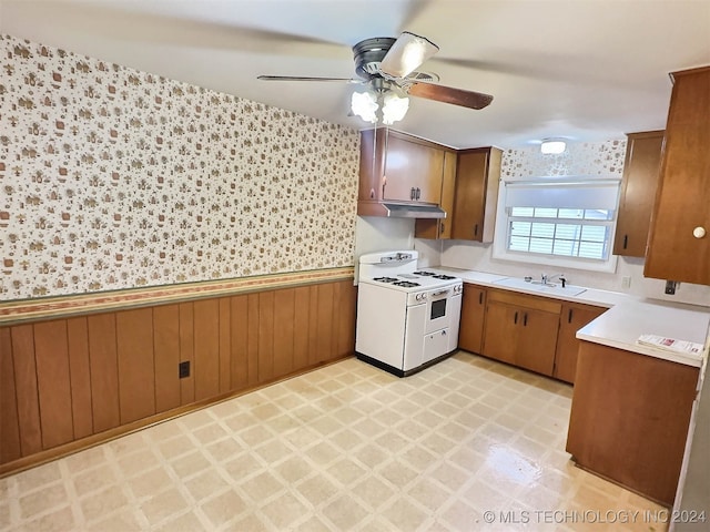 kitchen with electric range, ceiling fan, wood walls, and sink