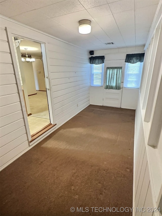 carpeted empty room featuring a notable chandelier, a healthy amount of sunlight, and wooden walls