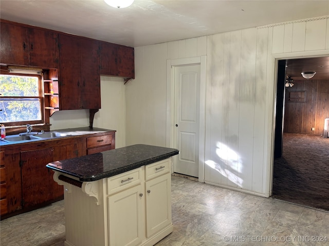 kitchen featuring ceiling fan, sink, cream cabinetry, wooden walls, and a breakfast bar