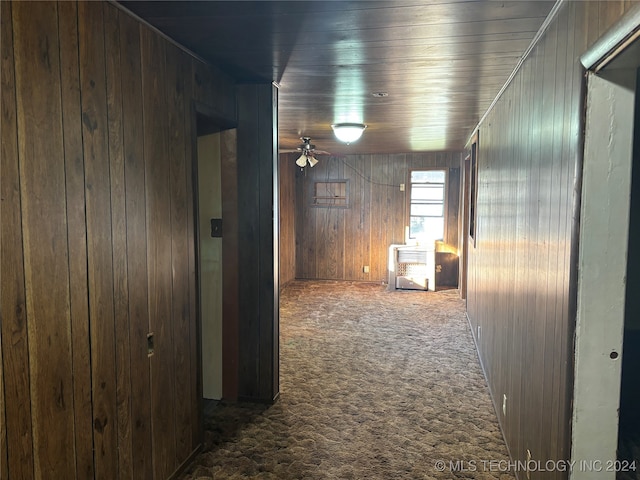 hall with wood walls and dark colored carpet