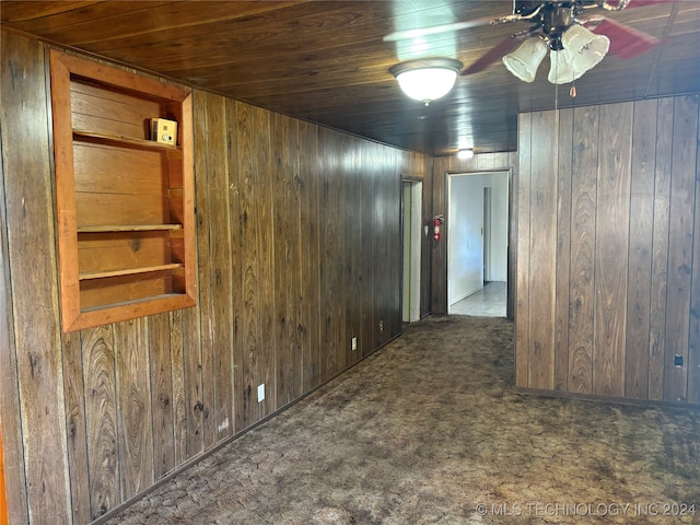 spare room with wooden walls, ceiling fan, dark carpet, and wooden ceiling