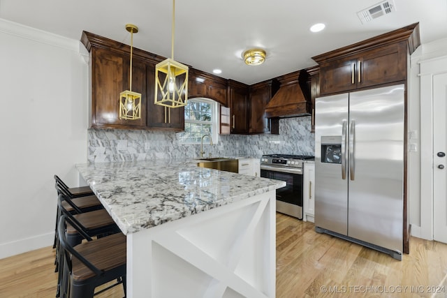 kitchen featuring appliances with stainless steel finishes, premium range hood, a breakfast bar, light hardwood / wood-style floors, and hanging light fixtures