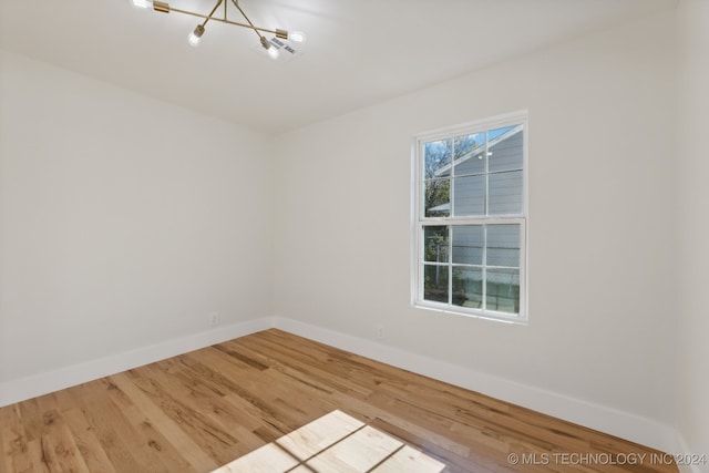 spare room with hardwood / wood-style floors and an inviting chandelier