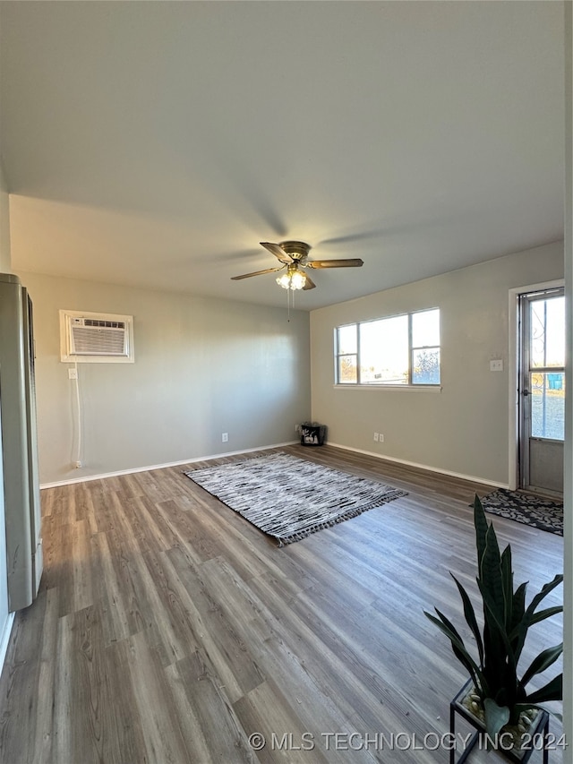 unfurnished living room featuring a wall mounted AC, ceiling fan, plenty of natural light, and wood-type flooring