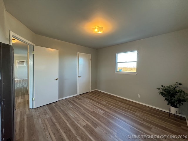 unfurnished bedroom with a wall unit AC, a closet, refrigerator, and wood-type flooring