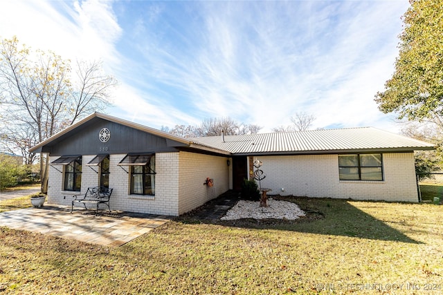 rear view of property featuring metal roof, a yard, brick siding, and a patio area