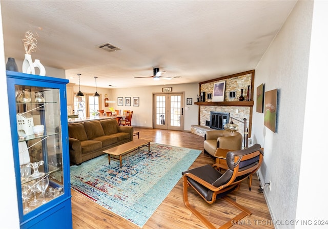 living room with a stone fireplace, a wealth of natural light, ceiling fan, and hardwood / wood-style flooring