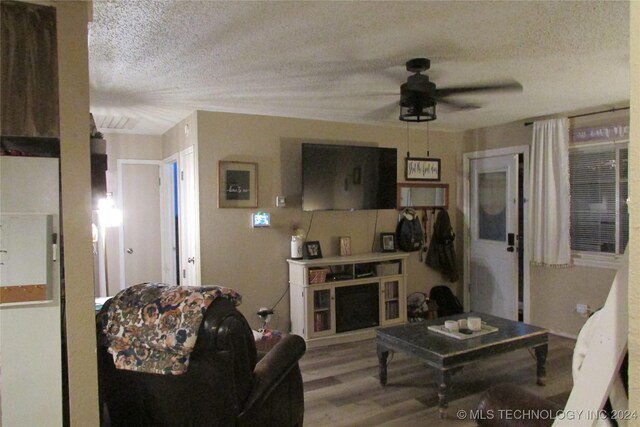 living room featuring hardwood / wood-style flooring, ceiling fan, and a textured ceiling