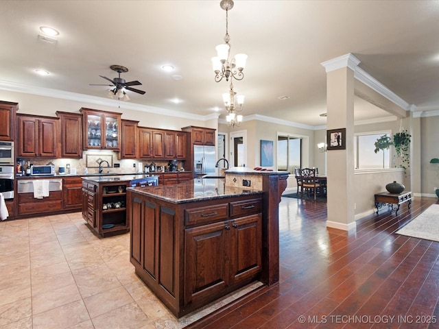kitchen with dark stone countertops, decorative backsplash, stainless steel appliances, and an island with sink