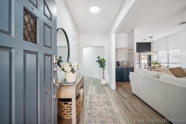 foyer with a textured ceiling, light wood-type flooring, and an inviting chandelier