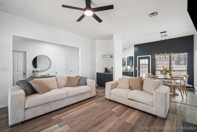 living room featuring a textured ceiling, dark wood-type flooring, and ceiling fan with notable chandelier