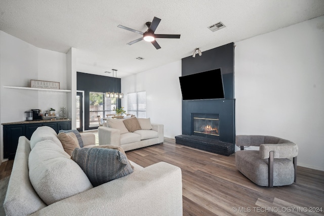 living room featuring ceiling fan with notable chandelier, wood-type flooring, and a textured ceiling