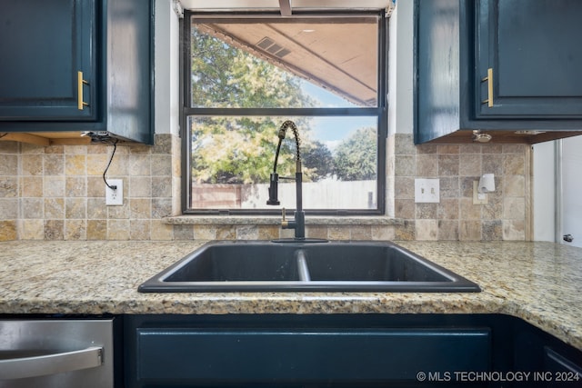 kitchen featuring light stone countertops, backsplash, blue cabinets, and sink