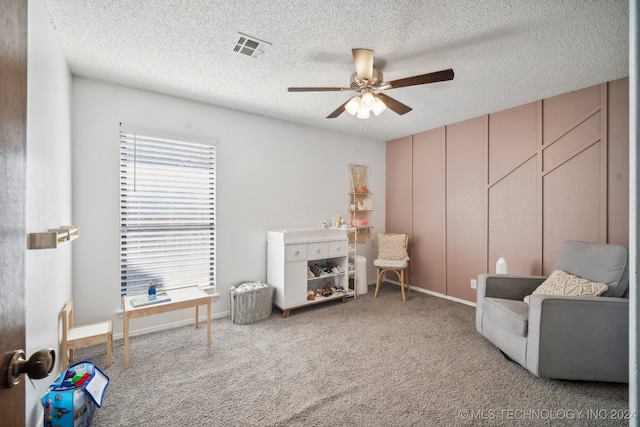 living area featuring carpet, ceiling fan, and a textured ceiling