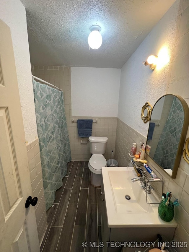 bathroom with vanity, toilet, tile walls, and a textured ceiling