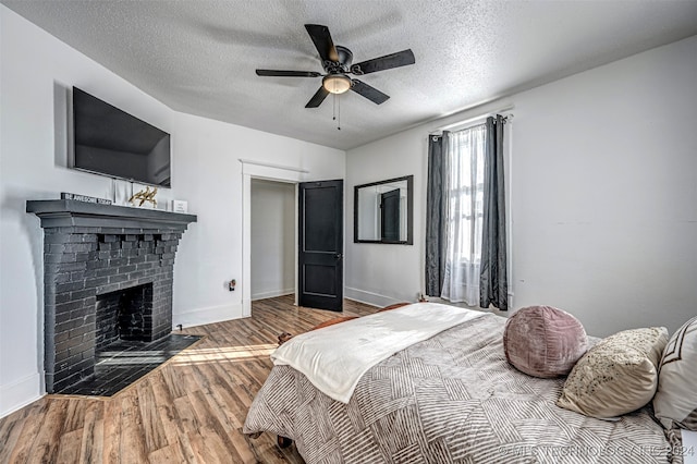 bedroom with ceiling fan, a fireplace, light wood-type flooring, and a textured ceiling