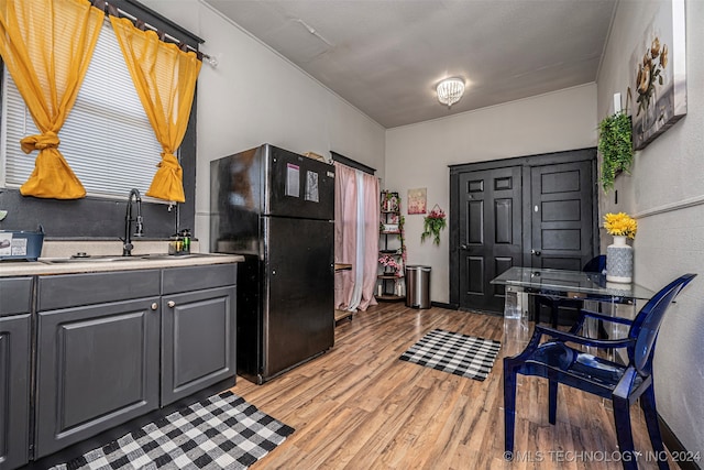 kitchen featuring gray cabinetry, black fridge, sink, and light hardwood / wood-style flooring