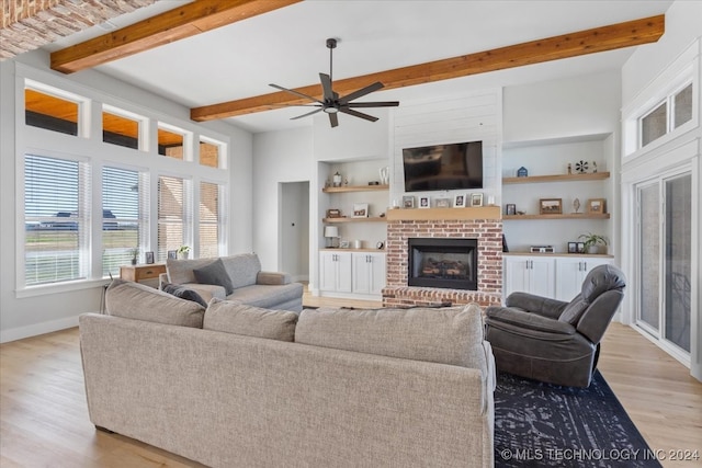 living room featuring ceiling fan, a fireplace, beamed ceiling, and light wood-type flooring